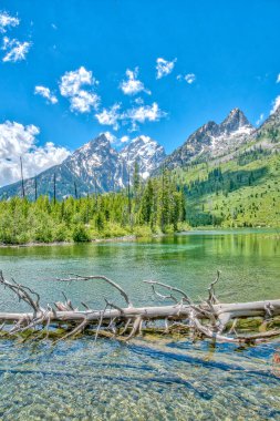 Önünde göl olan güzel bir dağ sırası. Su berrak ve sakin, gölün etrafındaki ağaçlar yemyeşil ve yemyeşil. Huzurlu ve huzurlu bir sahne.
