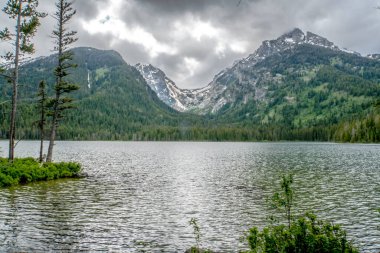 Arkasında dağlar olan bir göl. Gökyüzü bulutlu ve su sakin. Huzurlu ve huzurlu bir sahne.