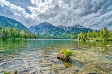 Arkasında dağlar olan bir göl. Gökyüzü bulutlu ve su sakin.