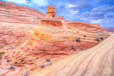 Arkasında küçük bir tepe olan büyük bir kaya oluşumu. Kaya oluşumu turuncu ve kahverengidir.
