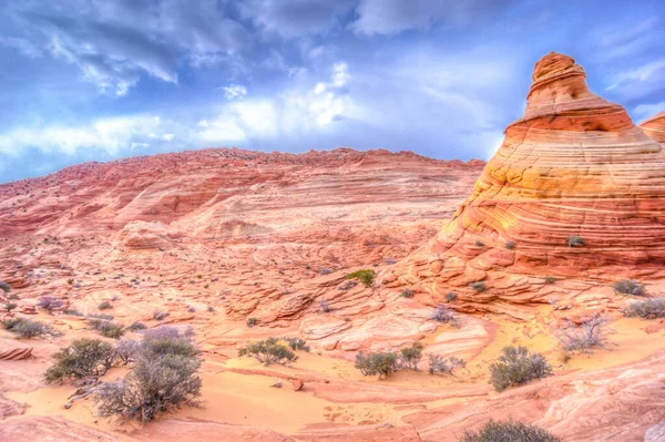 Uzakta büyük bir kaya oluşumu olan bir çöl manzarası. Gökyüzü bulutlu ve güneş batıyor.