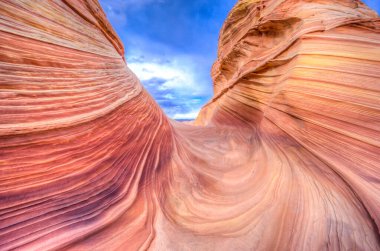 Görüntü derin, dolambaçlı bir yolu olan bir kanyonun görüntüsü. Kanyon taşlarla dolu ve kırmızımsı turuncu bir renge sahip. Kanyonun üstündeki gökyüzü açık ve mavi.
