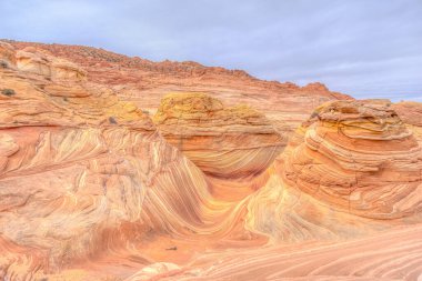 Ortasında büyük, derin bir kanyon olan kayalık, çöl manzarası. Gökyüzü bulutlu ve güneş görünmüyor.