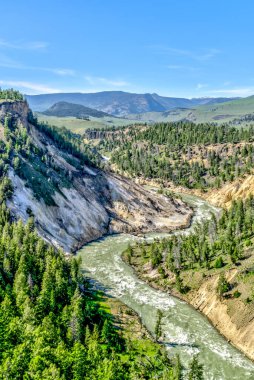 Arkasında dağlar olan yemyeşil bir vadi boyunca akan bir nehir. Su kristal gibi berrak ve manzara nefes kesici.