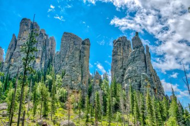 Dağlar ağaçlarla kaplı ve gökyüzü mavi. Dağlar çok yüksek ve ağaçlar yeşil.