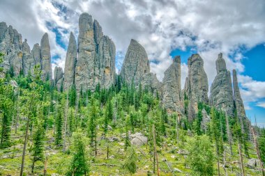 Birkaç ağacı ve bulutlu gökyüzü olan bir dağ sırası. Ağaçlar yeşil ve gökyüzü mavi.