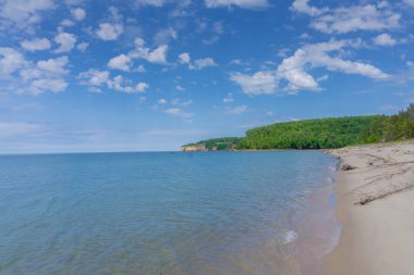 Açık mavi bir okyanusu ve arkasında yeşil bir tepesi olan güzel bir sahil. Gökyüzü çoğunlukla açık ve birkaç bulut etrafa saçılmış. Sahne sakin ve sakin, sakin okyanusla