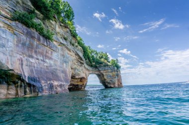 Arka planda büyük bir kaya duvarı olan güzel mavi bir okyanus. Su sakin ve gökyüzü berrak.