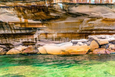 Önünde bir su kütlesi olan kayalık bir kıyı şeridi. Su yeşil ve kayalar kahverengi.