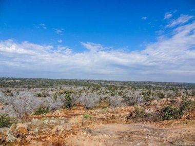 Açık mavi gökyüzü olan çorak bir çöl manzarası. Gökyüzü bulutlarla kaplı. Sahneye derinlik ve atmosfer hissi veriyor.