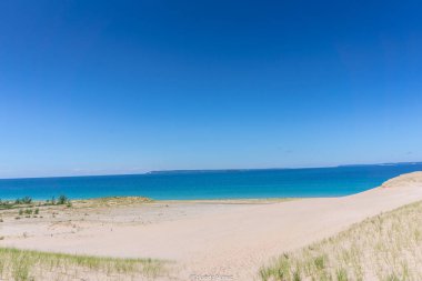 Mavi okyanusu ve açık gökyüzü olan bir sahil. Kumsal boş ve su sakin.