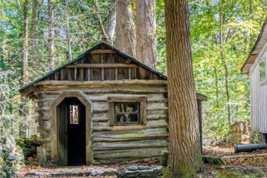 Penceresi ve kapısı olan küçük bir ahşap kulübe. Kulübe ağaçlarla çevrili ve kırsal bir havası var.