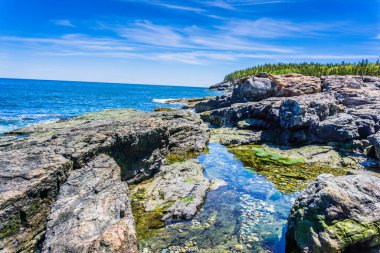 Ortasında küçük bir su kütlesi olan kayalık bir kıyı şeridi. Su berrak ve sakin, ve gökyüzü mavi. Huzurlu ve huzurlu bir sahne.