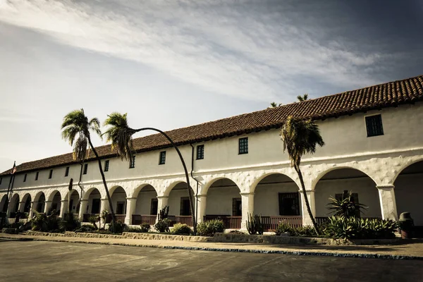 Kemerli camları ve beyaz çatısı olan büyük bir bina. Bina palmiye ağaçlarıyla çevrili.