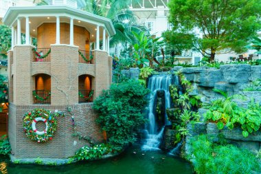 Üzerinde çelenk olan küçük bir tuğla bina bir şelalenin yanında yer alır. Şelale yemyeşil bitkiler ve ağaçlarla çevrilidir. Sahne huzurlu ve sakin, suyun sesiyle.