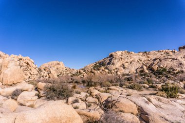 Açık mavi gökyüzü olan kayalık bir çöl manzarası. Gökyüzü çok parlak ve güneş parlıyor.