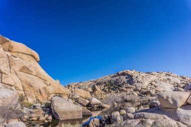 Açık mavi gökyüzü olan kayalık bir arazi. Gökyüzü çok parlak ve güneş parlıyor.
