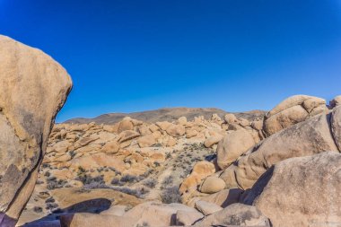 Arka planda mavi gökyüzü olan kayalık bir çöl manzarası. Kayalar bölgenin dört bir yanına dağılmış, bazıları daha büyük, bazıları daha küçük. Huzurlu ve huzurlu bir sahne.