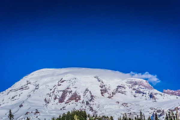 Arkasında mavi gökyüzü olan karla kaplı bir dağ. Dağ çok yüksek ve kar çok beyaz.