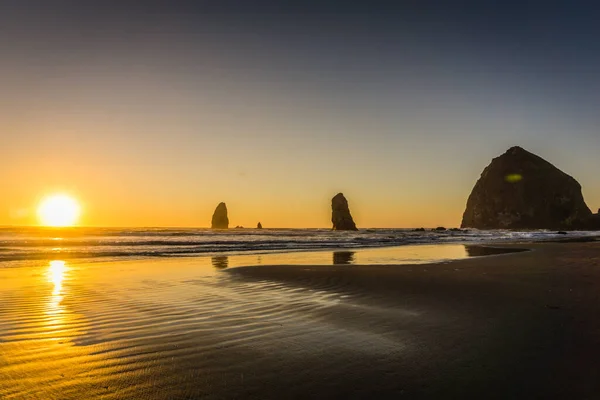 Güneş okyanusun üzerinde batıyor, kumsalda sıcak bir parıltı yayıyor. Dalgalar yavaşça kıyıya vuruyor ve gökyüzü turuncu ve pembe renklerin güzel bir karışımı. Sahne huzurlu ve huzurlu.