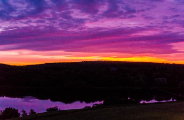 Gölün üzerinde güzel bir günbatımı. Suyun üzerinde gökyüzünün yansıması. Gökyüzü mor ve turuncu renklerin karışımıdır. Huzurlu ve huzurlu bir atmosfer yaratır.