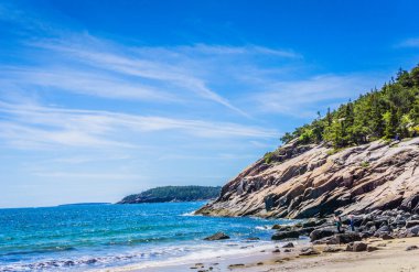 Arkasında kayalık bir uçurum olan güzel bir sahil. Gökyüzü açık ve mavi, ve su sakin