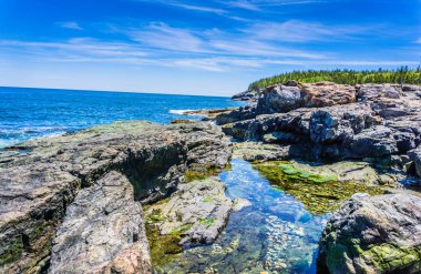 Ortasında küçük bir su kütlesi olan kayalık bir kıyı şeridi. Su berrak ve sakin, ve gökyüzü mavi. Huzurlu ve huzurlu bir sahne.
