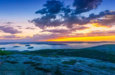 Arka planda dağlar olan bir gölün üzerinde güzel bir günbatımı. Gökyüzü bulutlarla dolu ve güneş batıyor. Sıcak ve huzurlu bir atmosfer yaratıyor.