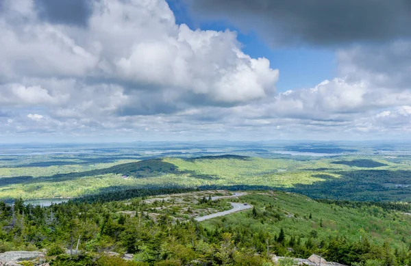 Bulutlu bir gökyüzü ve birkaç ağacı olan bir dağ manzarası. Gökyüzü mavi ve bulutlar beyaz