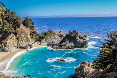 Kayalık bir kıyı şeridi olan güzel mavi bir okyanus. Su sakin ve gökyüzü berrak.