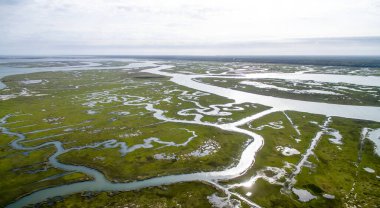 Büyük bir su kütlesi yeşil bir manzarayla çevrilidir. Su sakin ve gökyüzü bulutlu.
