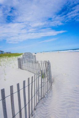 Beyaz çitli ve mavi plaj sandalyeli bir plaj. Kumsal boş ve gökyüzü mavi.