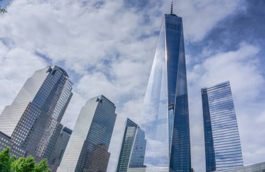 Sivri uçlu bir çatısı olan yüksek bir bina şehrin ufuk çizgisinin önünde duruyor. Gökyüzü bulutlu, ama güneş bulutların arasından parlıyor. Şehir hareketle dolup taşıyor.