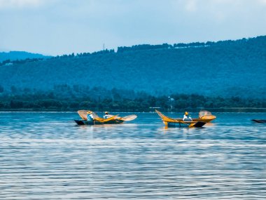 Bir gölde iki tekne yüzüyor, biri diğerinden daha büyük. Su sakin ve gökyüzü mavi. Sahne huzurlu ve huzurlu bir atmosfer veriyor.