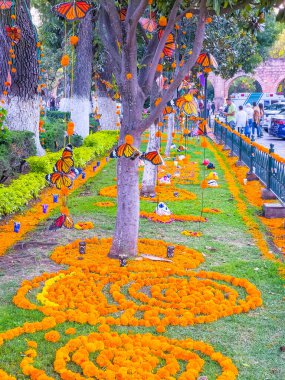 Bir ağaç portakal çiçekleri ve kelebeklerle süslenir. Çiçekler spiral bir düzende dizilmiş. Sahne kaldırımlı bir parkta geçiyor ve birkaç kişi geçiyor.