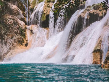 Bir şelale bir su kütlesine akıyor. Su berrak ve mavi. Şelale çok büyük ve su çok derin.