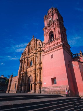 Saat kulesi olan büyük kırmızı bir bina. Bina bir avlu ile çevrili ve ona doğru giden merdivenler var.