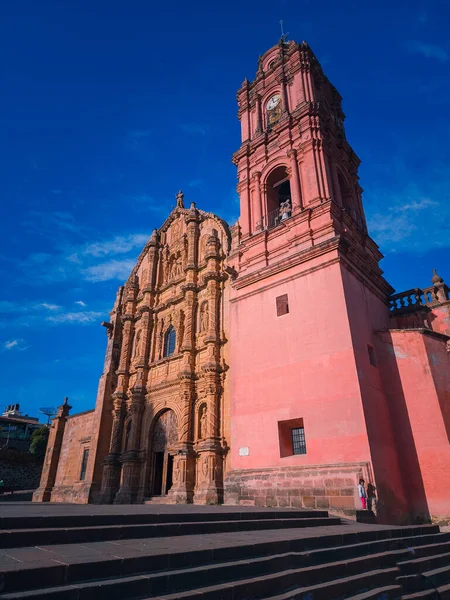 Saat kulesi olan büyük kırmızı bir bina. Bina bir avlu ile çevrili ve ona doğru giden merdivenler var.