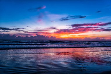 Sakin deniz, alacakaranlıkta parlayan ufukla buluşur. Yumuşak dalgalar ıslak kumda dalgalanır. Gökyüzü altın, pembe ve menekşe rengi ile kızarır. Bulutlar incelmiş, solgun güneş tarafından boyanmış.