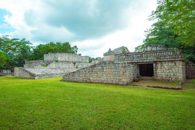 Kadim taş kalıntıları bulutlu gökyüzünün altında duruyor. Bereketli yeşil çimenler yıpranmış taş duvarları kuşatır. Uzun ağaçlar tarihi yapıyı yumuşakça çerçeveler. Açık kapı merakı ve merakı davet eder.