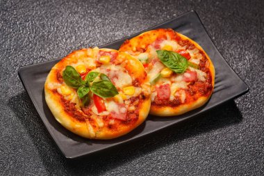 Erimiş peynir ve siyah tabakta taze fesleğenle kaplı iki lezzetli mini pizza sergileniyor..