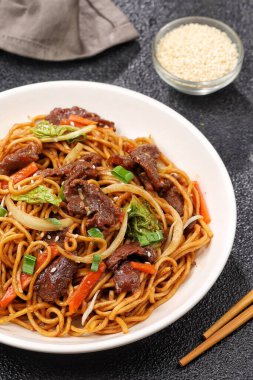 Bir tabakta sığır eti, kızarmış erişte, taze et dilimleri ve baharatlı soslu karışık sebzeler servis ediliyor.