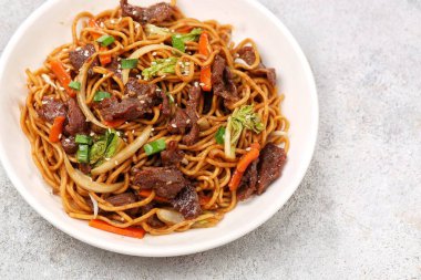 Bir tabakta sığır eti, kızarmış erişte, taze et dilimleri ve baharatlı soslu karışık sebzeler servis ediliyor.