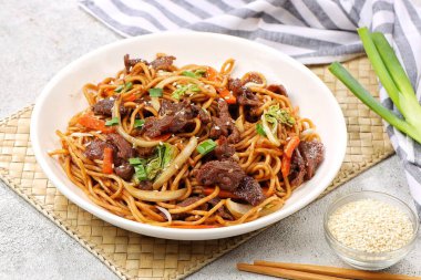 Bir tabakta sığır eti, kızarmış erişte, taze et dilimleri ve baharatlı soslu karışık sebzeler servis ediliyor.