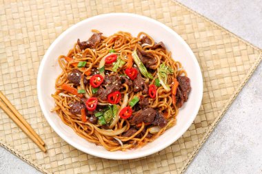 Bir tabakta sığır eti, kızarmış erişte, taze et dilimleri ve baharatlı soslu karışık sebzeler servis ediliyor.