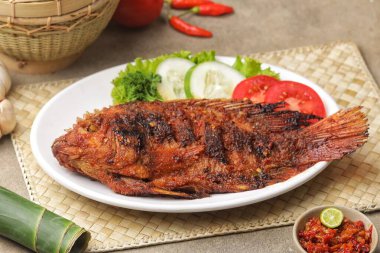 Izgara balık, beyaz tabakta sebze ve biber sosuyla servis edilir.