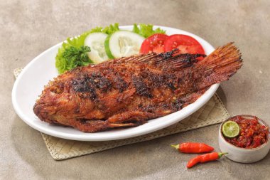 Beyaz tabakta salata, limon ve kırmızı biberle süslenmiş balık pişirdim.