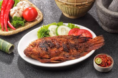 Izgara balık taze sebze ve meze ile beyaz tabakta servis edilir.