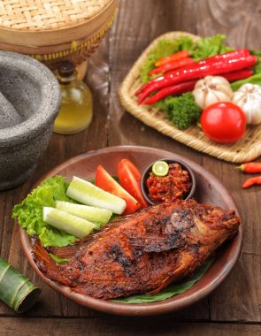 Dilimlenmiş salatalık, domates ve ahşap masada taze otlarla servis edilen ızgara balık..