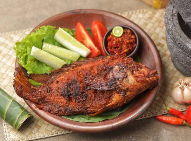 Kahverengi tabakta sebze ve sosla servis edilen ızgara balık.